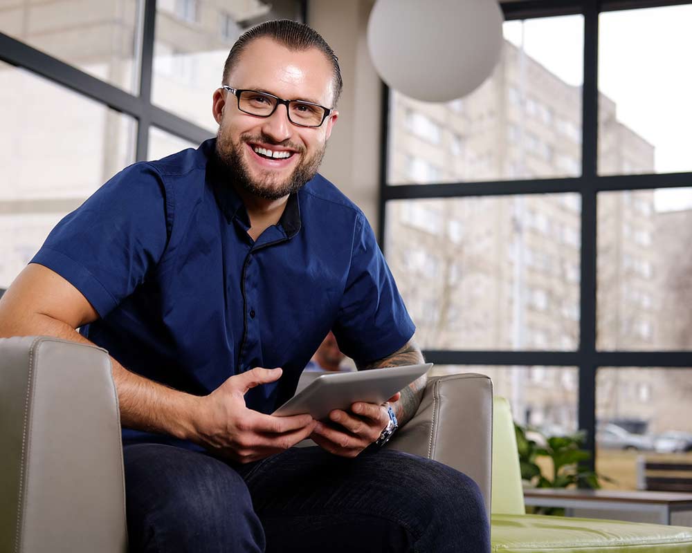 Man sitting in chair, holding tablet, smiling at camera | Featured image on Horizon Wealth Brisbane Financial Advisors home page.
