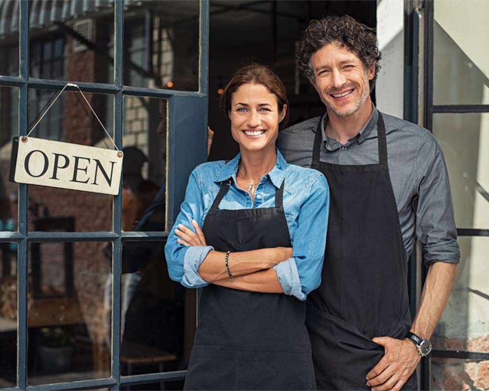 A couple, likley business owners, smiling and standing in-front of their business | Featured image on Horizon Wealth Brisbane Financial Advisors home page.