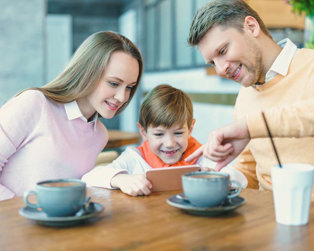 Family sitting at cafe with son, pointing to phone