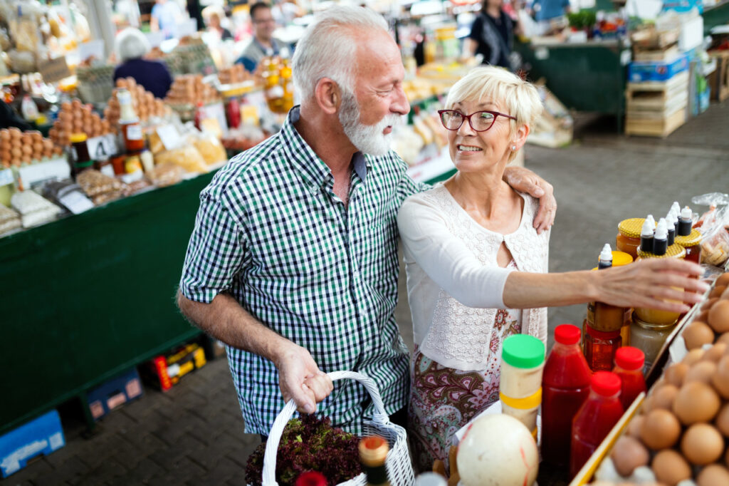 Smiling senior couple holding basket with vegetables at the market | Featured image for Inflation and Retirement Planning blog.